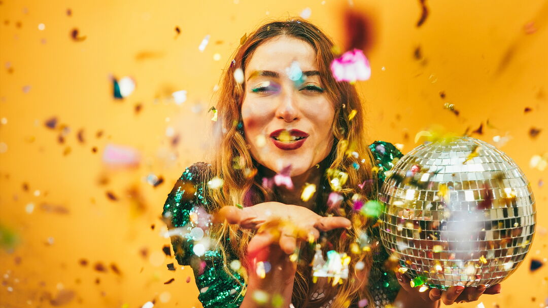 Fröhliche Frau mit Discokugel pustet Glitterkonfetti